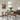 Eetkamer met glazen tafel, houten stoelen, moderne hanglamp, groene plant, schilderij aan muur.