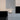 Driehoekige tafellamp, modern design, wit licht, minimalistisch interieur, zwart-wit contrast.