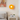 Oranje wandlamp in moderne slaapkamer, naast bed en nachtkastje met plant en boeken.