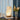 Moderne tafellamp met golvend ontwerp, warm licht, op houten basis, naast bloemenvaas.