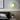 Groene wandlamp in moderne slaapkamer, naast zwart-wit kunstwerk en plant op nachtkastje.