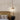 Hanglamp van beton en hout boven bed met rotan hoofdeinde, moderne slaapkamerinrichting.