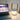 Draagbare LED tafellamp met handvat, modern design, wit en goud, naast laptop op tafel.