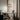 Glazen hanglamp boven moderne zwarte bureau met laptop en stoel, houten vloer, gordijnen.