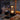 Hand houdt zwarte draagbare LED-lamp vast op houten tafel met herfstbladeren en mandarijnen.