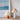Twee geplooide tafellampen, oranje en wit, naast Monet-poster op beige tafel.