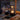 Hand houdt zwarte draagbare LED-lamp vast op houten tafel met herfstbladeren en sinaasappels.
