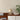 Beige tafellamp op houten kast met open boek en plant, moderne interieurdecoratie.