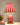 Rood-witte gestreepte tafellamp, circusstijl, decoratief, naast plant en boeken.