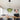 Groene glazen hanglamp boven houten eettafel in moderne woonkamer met grijze bank en kunst aan de muur.