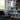Staande lamp met witte kap naast boekenkast en blauwe stoel in moderne woonkamer.