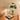Tafellamp met gouden voet en glazen kap naast groene plant op houten dressoir.