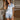 Vrouw in lichtblauw satijnen pyjama met korte mouwen en hartdetail, elegante slaapkameromgeving.